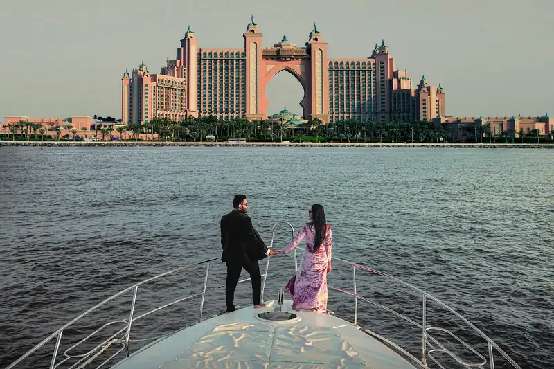 A couple on the bow of a yacht with the Atlantis hotel across the water behind them.