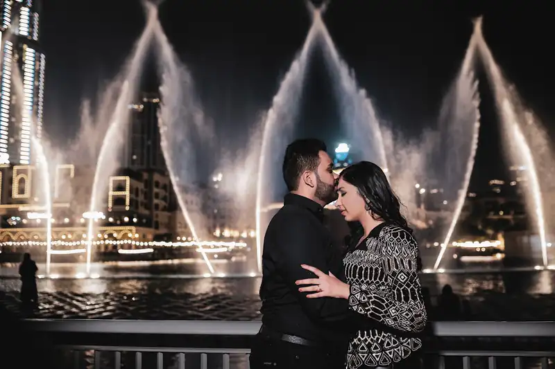 A couple in front of the lit Dubai fountain jets at night.