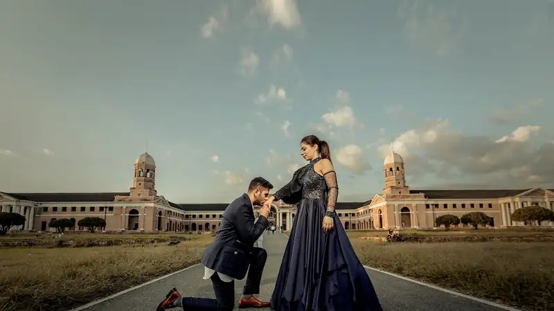 A man on one knee on a long empty road in front of a wide colonnaded building.